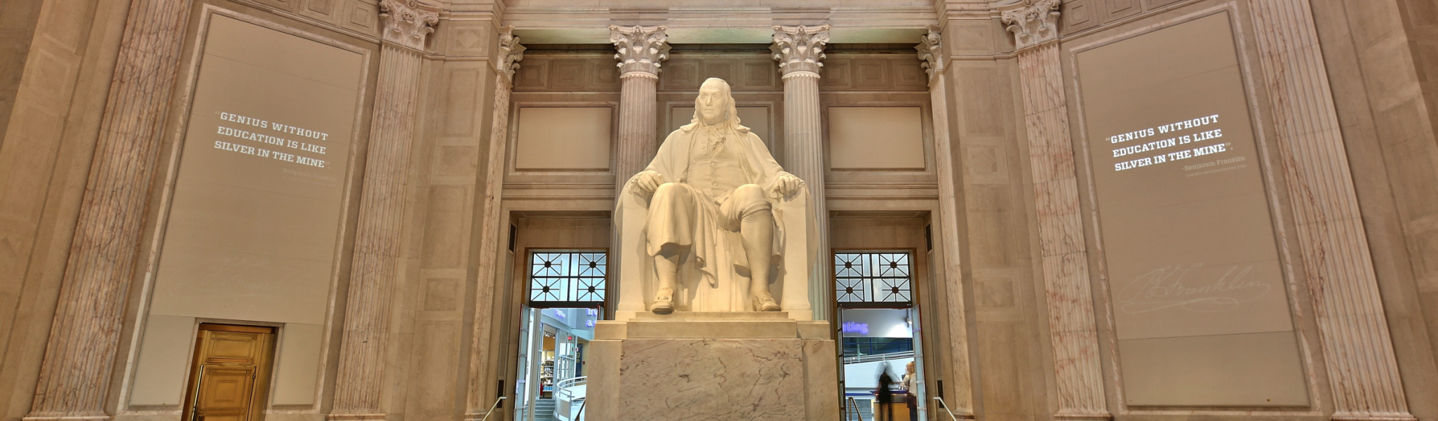 The Franklin Institute in Philadelphia with a statue of Benjamin Franklin in the center and the quote "Genius without education is like silver in the mine" on the wall to the left of the statue