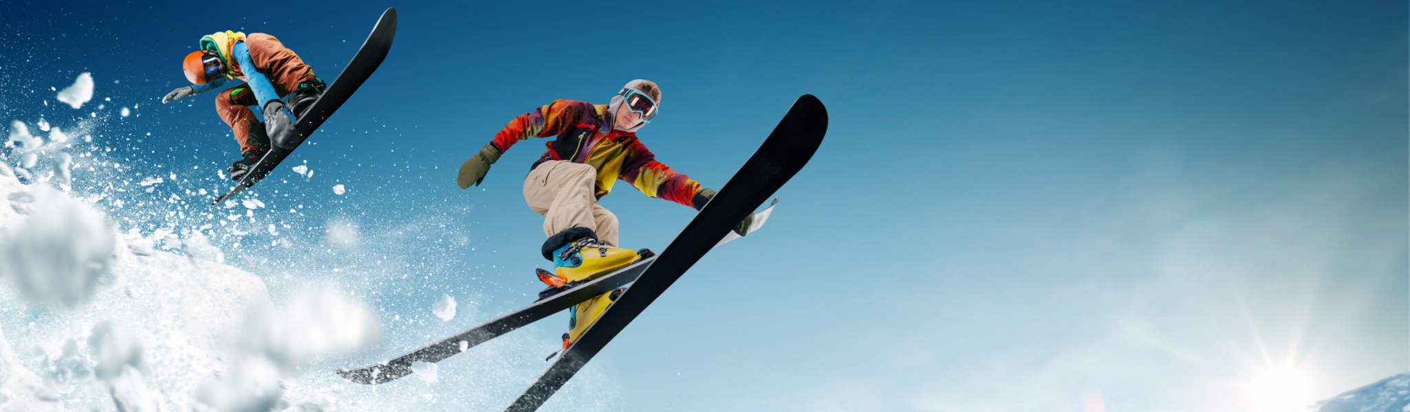 Skier and snowboarder catching some air with mountain peaks in the background